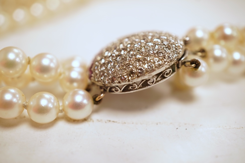 A cultured pearl, ruby and diamond clasp, composed of three rows of cultured pearls measuring approximately 6.9mm diameter, to a white precious metal (tests as 14k) disc-shaped clasp pavé-set with brilliant-cut diamonds